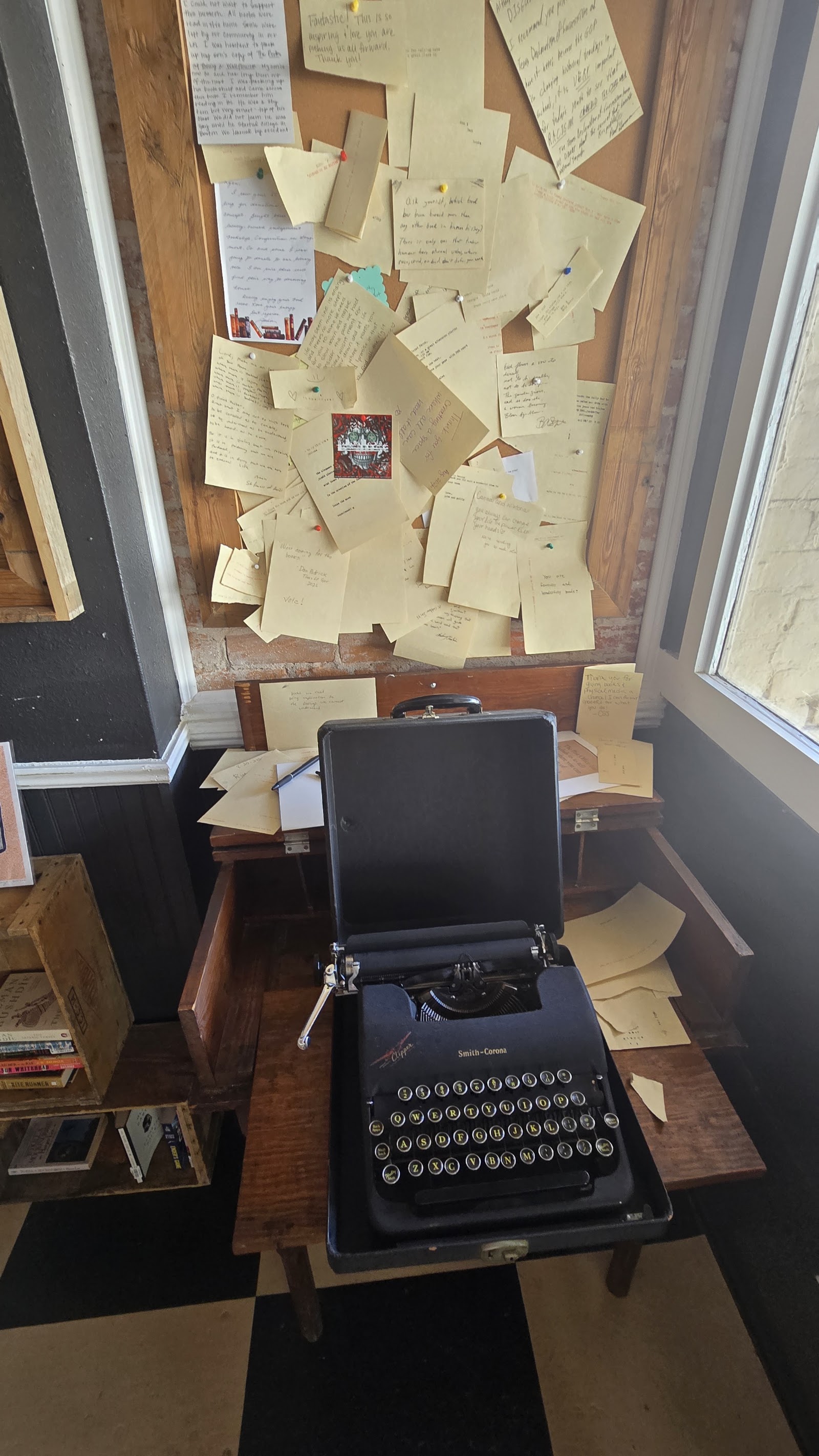 A vintage Smith-Corona typewriter on a stand beneath a wall of pinned handwritten notes